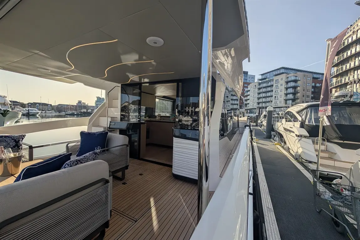 Modern yacht deck with stylish seating, marina views, and glass-panelled kitchen, showcasing luxury lifestyle by the water.